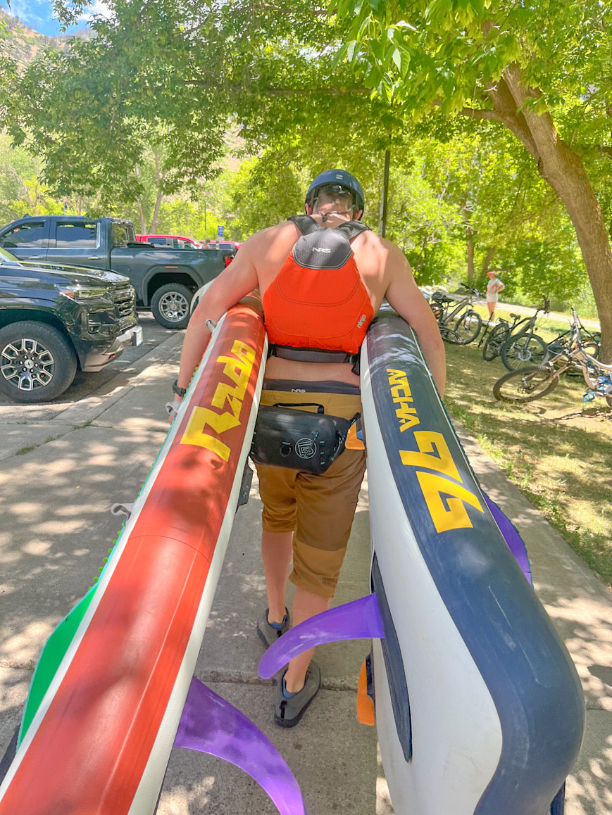 A group of five female paddleboarders in safety gear (helmets and PFDs) are standing next to their Hala stand-up paddleboards (SUPs) on a rocky riverbank.