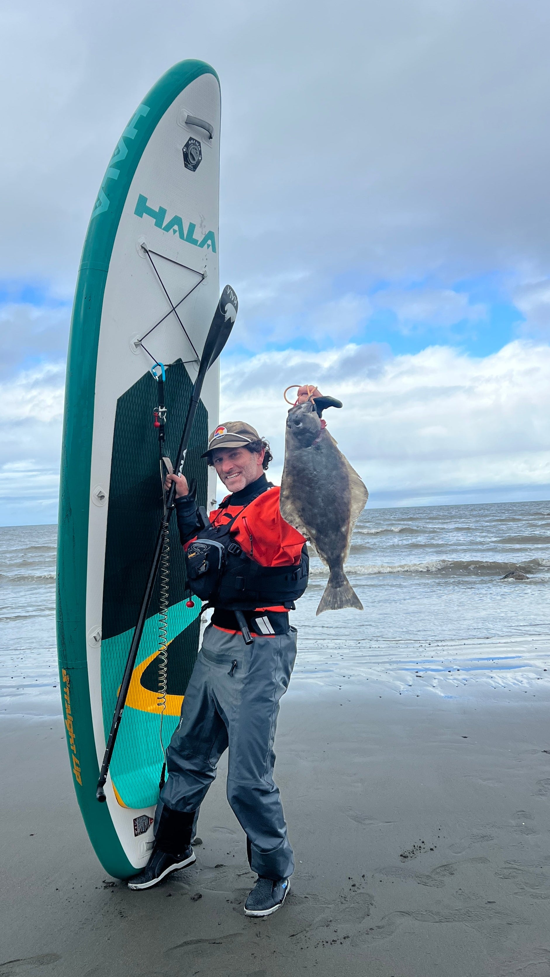 Person holding a fish and a paddleboard on a beach. Fishing from a Hala SUP board.